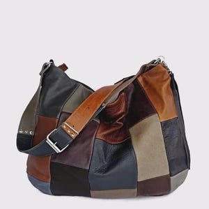 Könnte beinhalten: Eine große Patchwork-Leder-Umhängetasche in verschiedenen Braun-, Schwarz- und Grautönen. Die Tasche hat einen breiten, verstellbaren Riemen mit silberner Schnalle und Beschlägen. Die Tasche ist im Hobo-Stil.