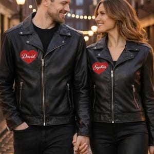 Puede incluir: Dos chaquetas de cuero negro a juego con parches de corazón rojo personalizados. Una chaqueta tiene bordado "David", la otra "Sophia". Ambas chaquetas presentan un estilo motero clásico con cremalleras y cuello con solapas.