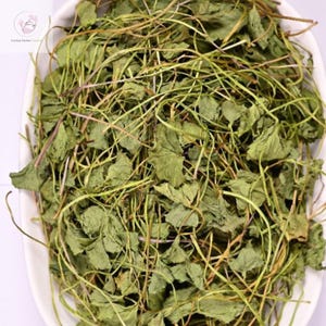 May include: A close-up of dried green leaves and stems in a white oval dish. The leaves have a textured appearance, and the stems are thin and wiry. The image highlights the natural details of the plant material.