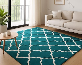 May include: Teal area rug with a white geometric pattern. The rug is rectangular and covers a large portion of the hardwood floor. A light-colored sofa and a small wooden table with decorative items are in the background.