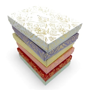 May include: A stack of six decorative gift boxes in various colours. The boxes are white, lavender, yellow, pink, red, and light green. Each box has a gold floral pattern on the lid. The boxes are stacked on top of each other.