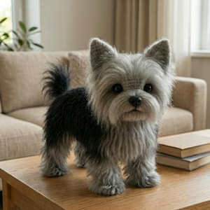 Puede incluir: Un juguete de peluche hecho a mano con forma de perro Yorkshire Terrier. El juguete tiene un esquema de color gris y negro, con textura de pelo detallada y ojos expresivos. Está sobre una mesa de madera.