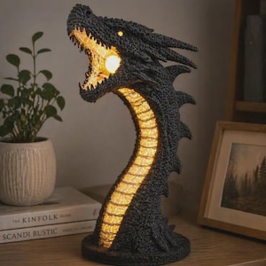 May include: A dark grey dragon lamp with an open mouth, emitting a warm, glowing light. The lamp's body curves upwards, with a textured surface and detailed design. The lamp is on a wooden surface.