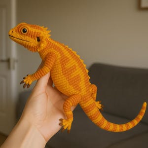 Peut inclure: Un dragon barbu crocheté aux tons orange et jaune. Le reptile fait main présente des écailles, des griffes et un dos épineux détaillés. Le lézard est tenu, mettant en valeur son corps entier et son design complexe.