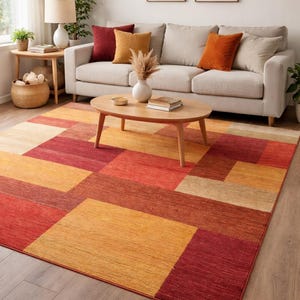 Könnte beinhalten: Ein rechteckiger Teppich mit einem geometrischen Blockmuster in den Farben Rot, Orange, Gelb und Beige. Der Teppich hat eine strukturierte Oberfläche und besteht aus großen, einfarbigen rechteckigen Abschnitten in einem Raster.