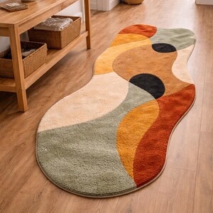 Luxury Modern Rug – Hand Tufted Rust & Beige Statement Rug for Home Decor. Abstract Hand Tufted Rug – Rust Red Beige Artistic Carpet for Living RoomAn abstract-shaped rug with a soft, textured surface. The rug features a design of overlapping shapes in shades of beige, orange, brown, green, and black. The rug is placed on a hardwood floor.
