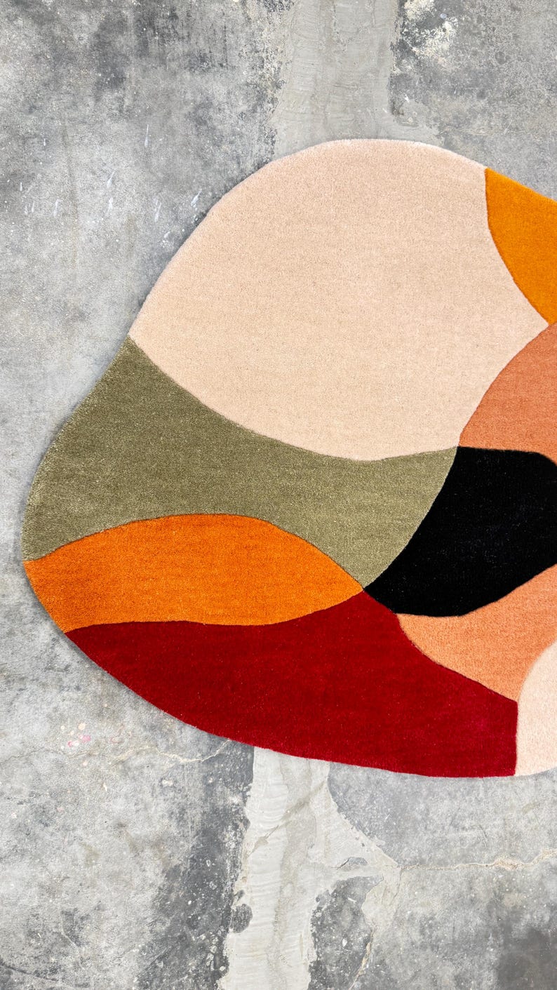 Soft Hand Tufted Wool Rug – Contemporary Rust Red Beige Living Room Ru. 
Designer Abstract Rug – Hand Tufted Rust Beige Carpet for Modern HomesA colorful, abstract rug with a unique, organic shape. The rug features a palette of warm colors, including red, orange, peach, and beige, contrasted with black and olive green. The design is modern and eye-catching, suitable for various interior styles.