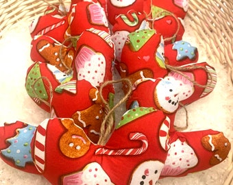 Puede incluir: Una colección de adornos en forma de corazón de fieltro rojo con un patrón de galletas navideñas. Los adornos presentan hombres de jengibre, bastones de caramelo, muñecos de nieve y cupcakes.