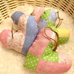 Pode incluir: Enfeites de tecido em forma de coração numa cesta de vime. Os corações de patchwork apresentam tecidos rosa, azul, verde e amarelo com estampados florais e de bolinhas. Cada coração tem uma argola de barbante para pendurar.
