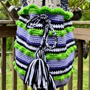 May include: A crocheted bag with green, purple, black, and white stripes. The bag has a drawstring closure and a black and white tassel.