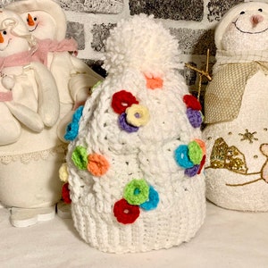 May include: White crocheted hat with a pompom on top. The hat is decorated with colorful crocheted flowers.