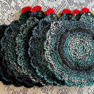 May include: Set of six crocheted black, teal, and white round coasters with a scalloped edge. Each coaster features a red and yellow crocheted chicken head.
