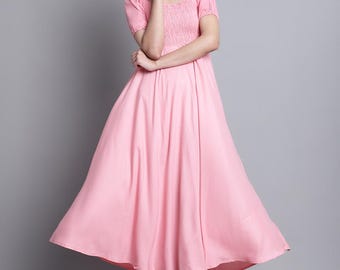 May include: A light pink dress with a square neckline and short sleeves. The bodice has a smocked design, and the skirt flares out. The dress is knee-length and worn with black sandals. The background is a solid gray.