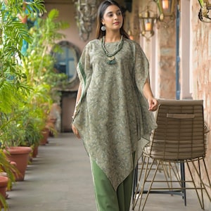 May include: A woman wearing a two-piece outfit. The top is a loose-fitting, olive green, floral-patterned tunic with a green trim. The pants are solid green with a white stripe down the side. She is also wearing a necklace and sandals.