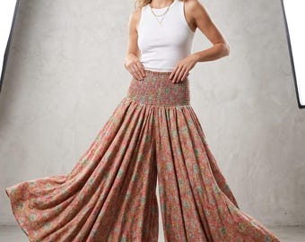 May include: A white sleeveless tank top paired with high-waisted, wide-leg trousers featuring a smocked elastic waistband. The trousers are patterned with a floral design in shades of muted orange, teal, and yellow, creating a full, flowing silhouette.