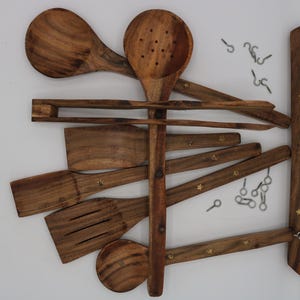 May include: Wooden kitchen utensil set, including spoons, spatulas, and a slotted spoon, arranged on a wooden rack with metal hooks. The utensils are a warm brown color, and the rack has decorative star-shaped accents.