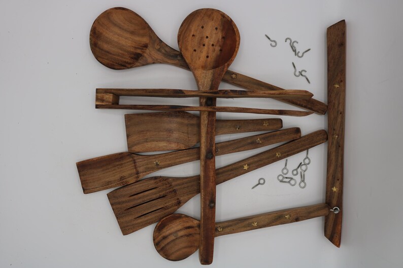 May include: Wooden kitchen utensil set, including spoons, spatulas, and a slotted spoon, arranged on a wooden rack with metal hooks. The utensils are a warm brown color, and the rack has decorative star-shaped accents.