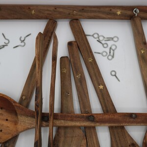May include: Wooden kitchen utensil set with a rack. The set includes a slotted spoon, spatulas, and other cooking tools. The rack and utensils are brown with brass star accents. Metal hooks are included for hanging.