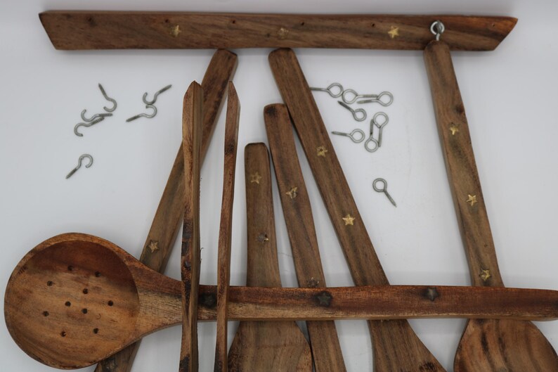 May include: Wooden kitchen utensil set with a rack. The set includes a slotted spoon, spatulas, and other cooking tools. The rack and utensils are brown with brass star accents. Metal hooks are included for hanging.