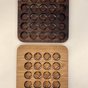 May include: Two wooden trays, one dark brown and one light brown, each with a grid of circular cutouts. The cutouts have a star-like pattern. The trays are square with rounded corners.