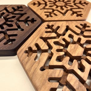 May include: Four hexagonal wooden coasters featuring snowflake designs. The coasters are crafted from wood in varying shades of brown. The snowflake patterns are cut out, offering a decorative and practical element for home use.