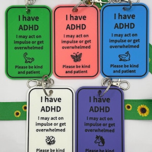 May include: Five rectangular plastic tags in green, coral, blue, white, and purple, each with a silver lobster clasp. The text reads: I have ADHD, I may act on impulse or get overwhelmed, Please be kind and patient. Each tag features a small icon.
