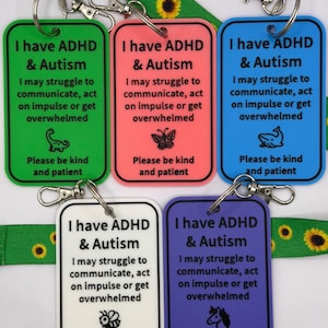 May include: Five rectangular plastic tags in green, pink, blue, white, and purple, each with a metal lobster clasp. The text reads: I have ADHD & Autism, I may struggle to communicate, act on impulse or get overwhelmed, Please be kind and patient.