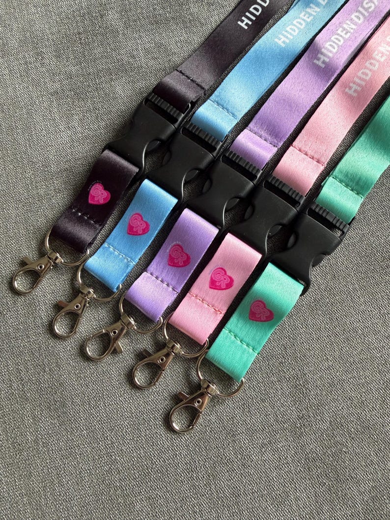Puede incluir: Cinco cordones en negro, azul claro, lavanda, rosa y verde menta, cada uno con el texto HIDDEN DISCO, una hebilla de liberaci&oacute;n lateral de pl&aacute;stico negro y un mosquet&oacute;n de metal plateado. Un peque&ntilde;o coraz&oacute;n rosa est&aacute; impreso en cada cinta.