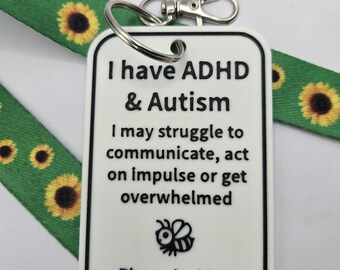 May include: A white rectangular tag with black text reading I have ADHD & Autism, I may struggle to communicate, act on impulse or get overwhelmed, Please be kind and patient, featuring a small bee icon, attached to a green sunflower lanyard.