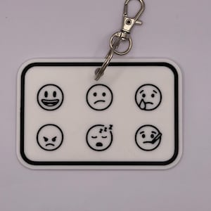 May include: White rectangular keyring with a black border, displaying six emoji faces: happy, sad, crying, angry, sleeping, and sick. It has a silver metal clasp.