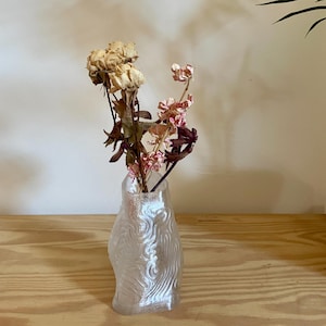Peut inclure: Un vase en verre transparent, texturé et de forme organique. Il contient des fleurs séchées beiges, roses et bordeaux. Posé sur une surface en bois clair, il crée une esthétique naturelle et minimaliste.