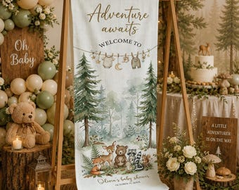 Peut inclure: Une bannière en tissu verticale avec le texte Adventure awaits WELCOME TO et Olivia's baby shower OCTOBER 11, 202X. Le motif présente des illustrations de pins, d'un renard, d'un cerf, d'un ours, d'un raton laveur et d'un écureuil.