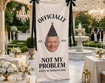 May include: A cream-colored banner with black text and accents, featuring a smiling man's face wearing a party hat. The banner reads "OFFICIALLY" above the face, "NOT MY PROBLEM" below, and "HAPPY RETIREMENT, BOB". Black bows secure the banner.