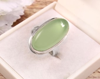 May include: A silver ring with a large, oval, pale green stone. The stone is set in a silver bezel and sits atop a silver band. The ring is displayed in a white jewelry box.