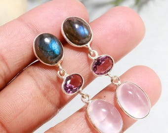 May include: A pair of silver earrings with a dangling design. Each earring features an oval labradorite stone at the top, followed by a smaller oval purple stone, and a larger oval pink stone at the bottom. The stones are connected by silver links.