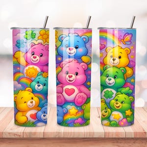 May include: Three stainless steel tumblers with colorful Care Bear designs. Each tumbler features a different arrangement of Care Bears, rainbows, and flowers. The tumblers have silver lids and straws, set on a wooden surface.