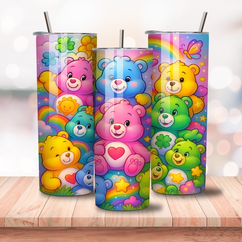 May include: Three stainless steel tumblers with colorful Care Bear designs. Each tumbler features a different Care Bear character, rainbows, and stars. The tumblers have a straw and a lid. The background is a blurred image of a wooden table.