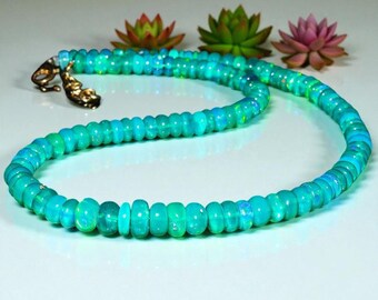 May include: A turquoise opal necklace with a gold clasp. The necklace is composed of round, polished opal beads in shades of blue and green. The beads are strung together to form a continuous loop. The background features decorative succulents.