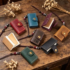 May include: A collection of small, leather-bound notebooks in various colors, including red, blue, and brown. Each notebook features a button closure and a decorative cord with beads. The notebooks are open and closed, showcasing the blank pages.
