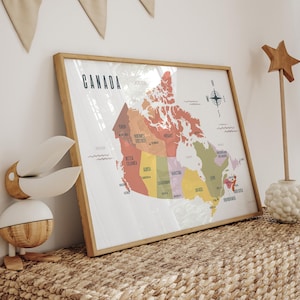 Könnte beinhalten: Eine gerahmte Karte von Kanada mit Holzrahmen. Die Karte ist nach Provinzen farbcodiert und enthält das Wort "KANADA" oben. Eine Windrose befindet sich in der oberen rechten Ecke. Die Karte wird auf einer gewebten Oberfläche angezeigt.