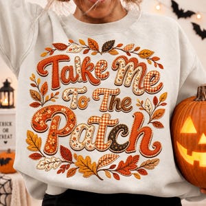 May include: A light gray crewneck sweatshirt featuring a graphic print with the text Take Me To The Patch in large, stylized orange and patterned letters. The design is surrounded by a circular arrangement of autumn leaves in shades of orange, red, and brown.