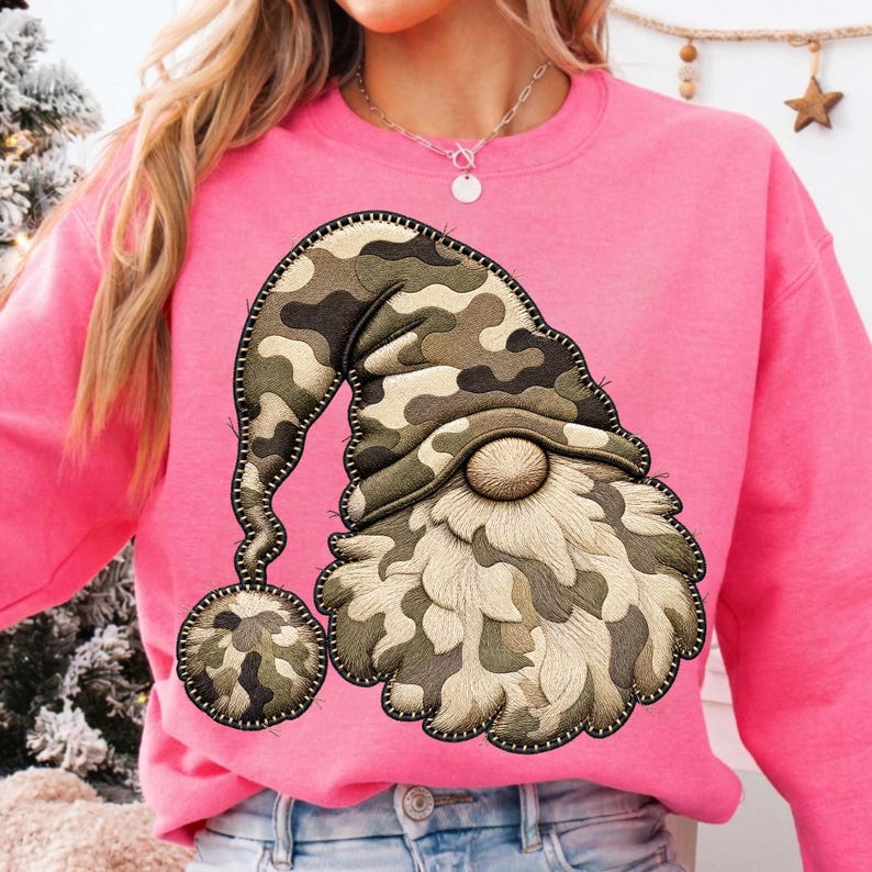 K&ouml;nnte beinhalten: Ein leuchtend pinkfarbenes Langarm-Sweatshirt mit einer gro&szlig;en, mittig aufgestickten Applikation eines Gnoms. Der Gnom tr&auml;gt eine M&uuml;tze mit Camouflage-Muster und passendem Bommel sowie einen strukturierten, cremefarbenen Bart und eine runde Nase.