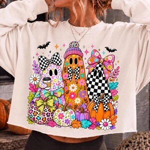 Puede incluir: Una sudadera de manga larga color crema con un estampado gr&aacute;fico colorido de tres fantasmas y tres calabazas. Los fantasmas est&aacute;n decorados con estampado de leopardo, motivos florales y lazos a cuadros. Las calabazas tienen flores y lazos.