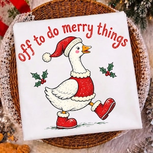 May include: A white t-shirt featuring a graphic of a goose wearing a red Santa hat, a red vest with white trim, and red boots. The goose is surrounded by two sprigs of holly with red berries. The text reads, off to do merry things, in red.