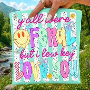 May include: A light mint green fabric square featuring a white vertical striped pattern with black dots. The text reads y'all were FERAL but i low key LOVE YOU in colorful, checkered, and solid fonts, accented by a yellow smiley face and flowers.