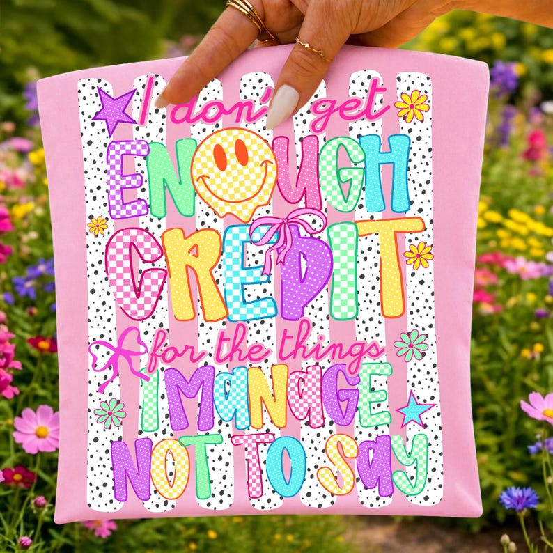Pode incluir: Um artigo de tecido rosa claro com um fundo de riscas de bolinhas pretas e brancas e texto colorido que diz I don't get ENOUGH CREDIT for the things I MANAGE NOT TO SAY, acentuado com uma cara sorridente amarela e pequenas flores.