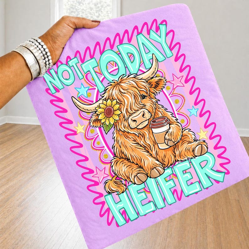 May include: A lavender blanket featuring a cartoon Highland cow with a sunflower and coffee cup. The text "NOT TODAY HEIFER" is in turquoise and pink, surrounded by stars and a wavy border. The blanket is held by a person.