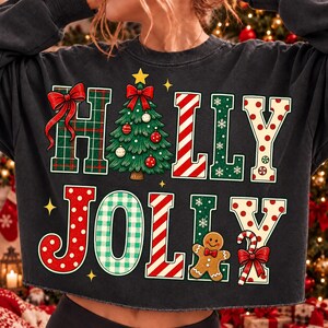 Peut inclure: Un sweat-shirt noir &agrave; manches longues avec le texte HOLLY JOLLY en grandes lettres color&eacute;es. Le H est &agrave; carreaux verts avec un n&oelig;ud rouge, le O est un sapin de No&euml;l, les L sont &agrave; rayures rouges, le Y est blanc &agrave; pois rouges et le J est rouge &agrave; pois.