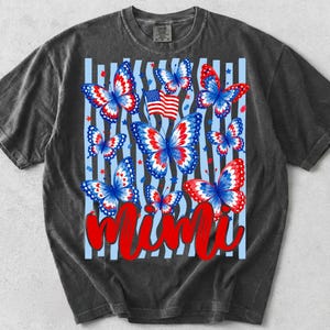 May include: A charcoal gray short-sleeve t-shirt featuring a graphic print of multiple butterflies with red, white, and blue wings. A small American flag is positioned among the butterflies, and the word Mimi is written in large red script.