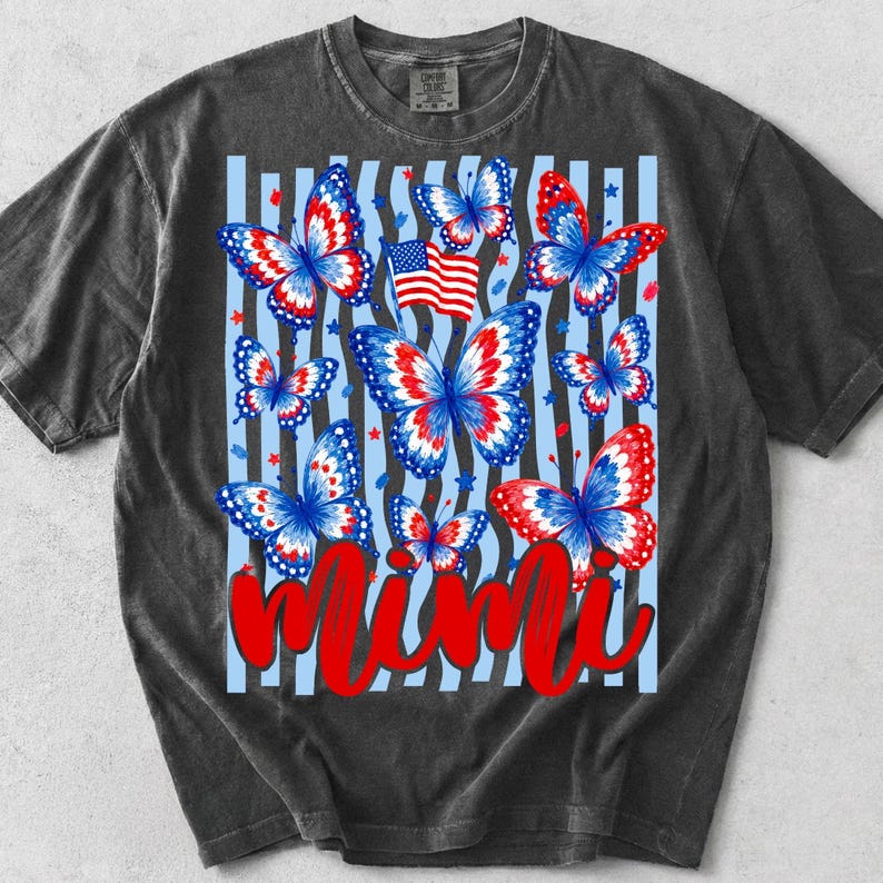 May include: A charcoal gray short-sleeve t-shirt featuring a graphic print of multiple butterflies with red, white, and blue wings. A small American flag is positioned among the butterflies, and the word Mimi is written in large red script.